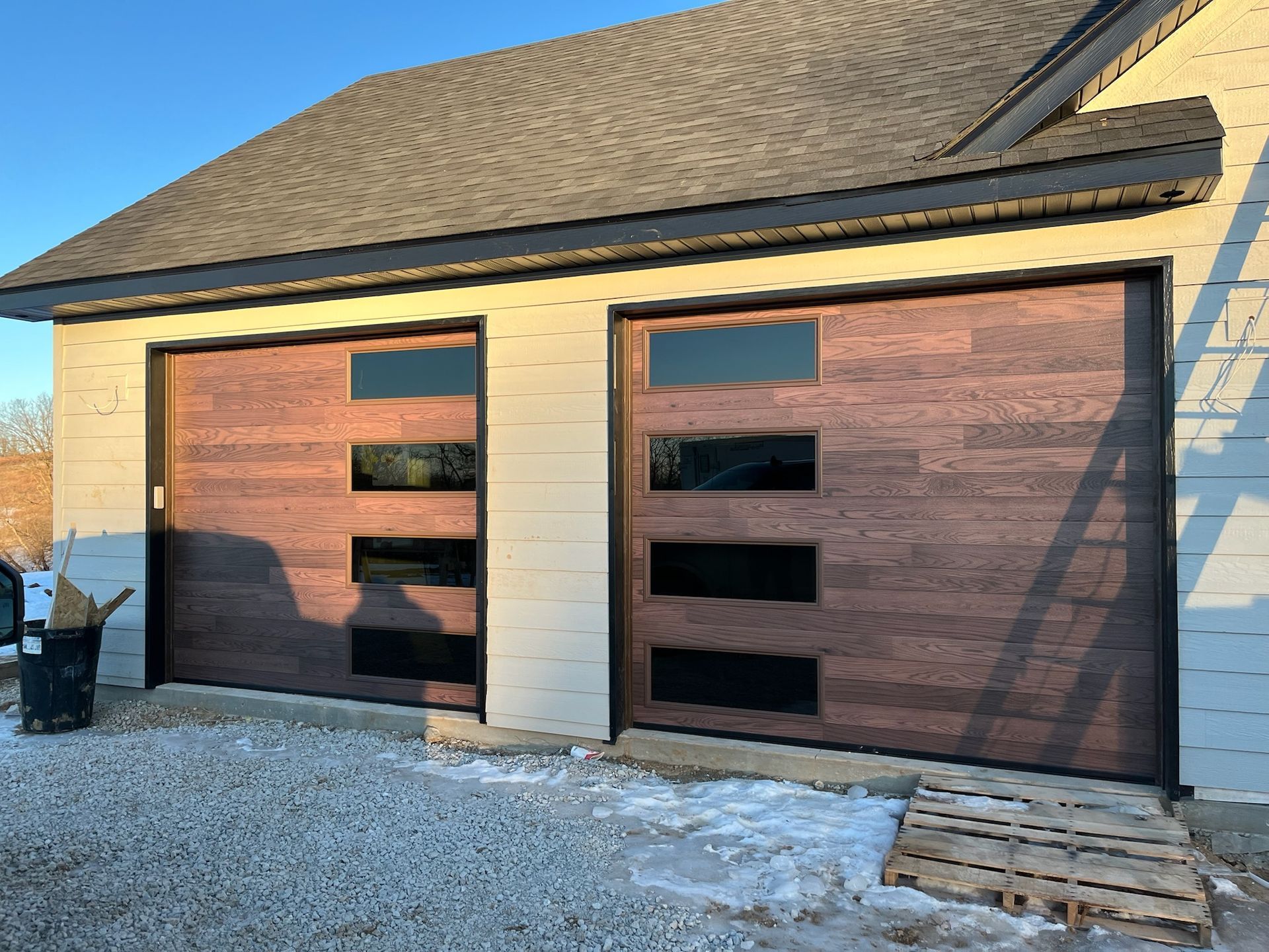Two matching garage doors with a brown wood-grain appearance, each with horizontal black windows.
