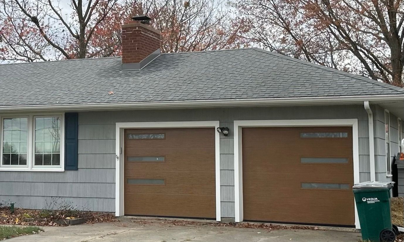 Exterior of a gray house with a roof and two brown garage doors.