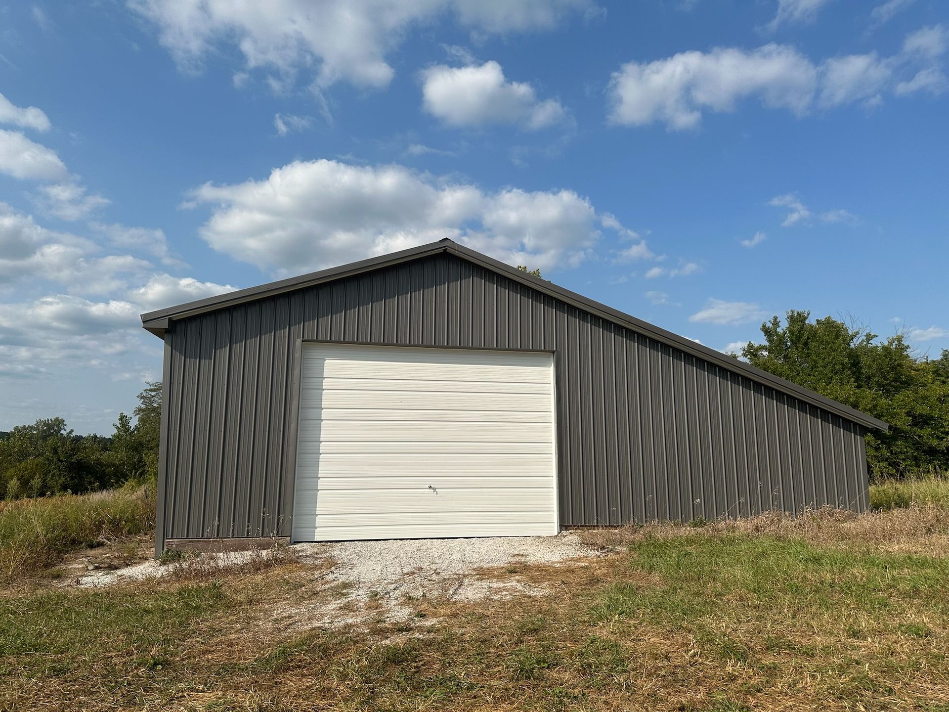 Gray shed with a white garage door, gravel base, and a blue sky with clouds.