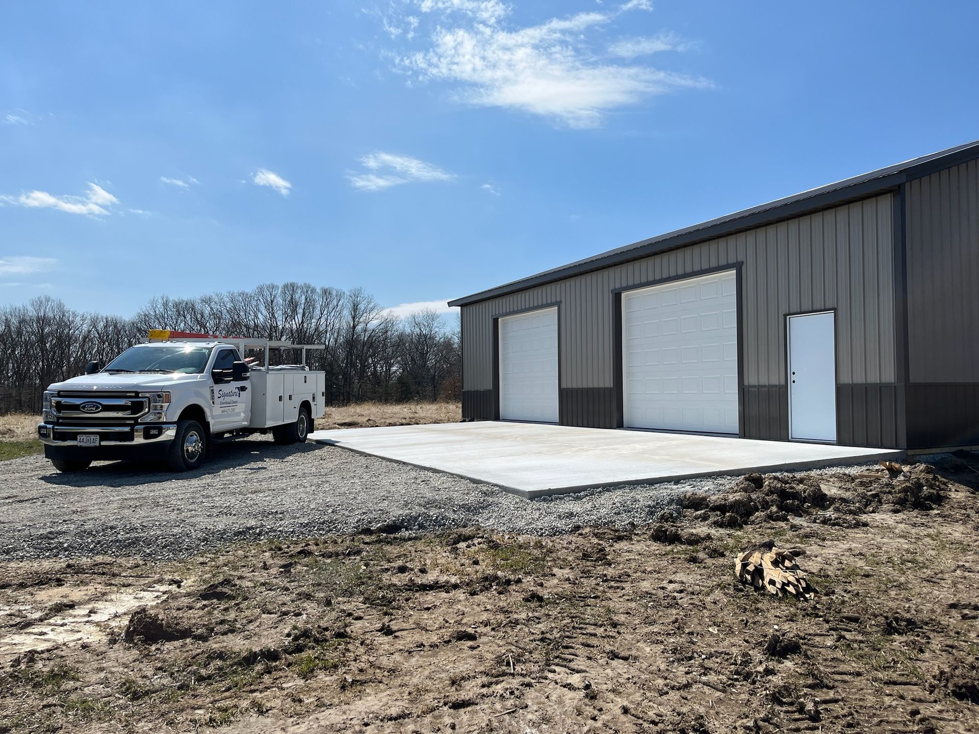 White work truck parked next to a gray and brown metal warehouse with closed garage doors on a sunny day.