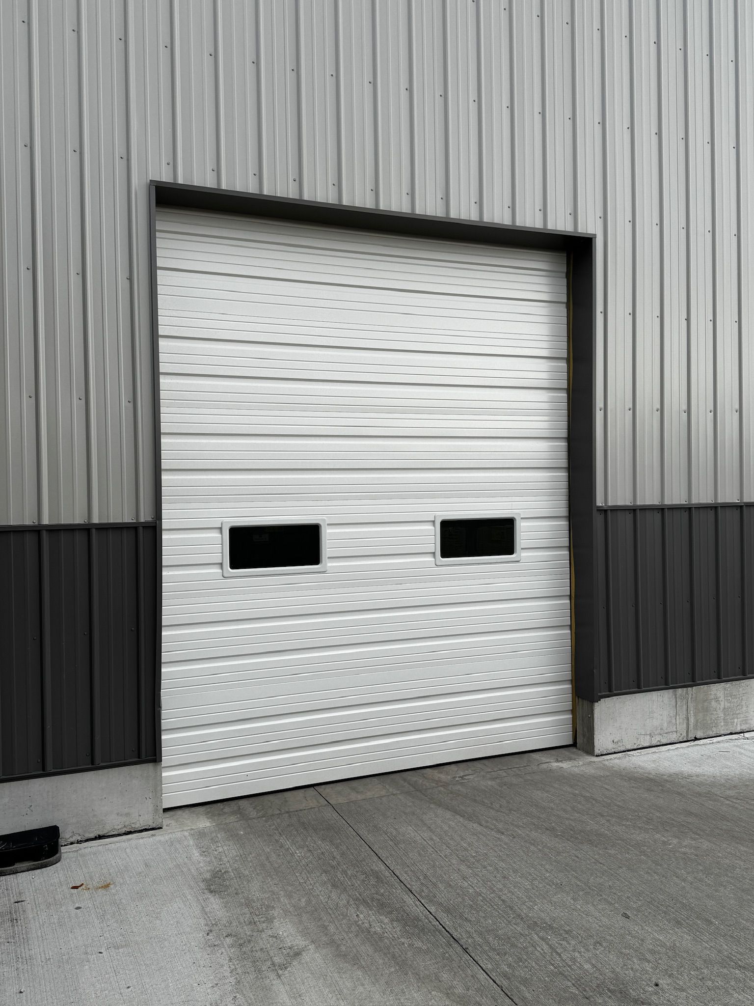 Closed white industrial garage door with two window openings in a metal building.