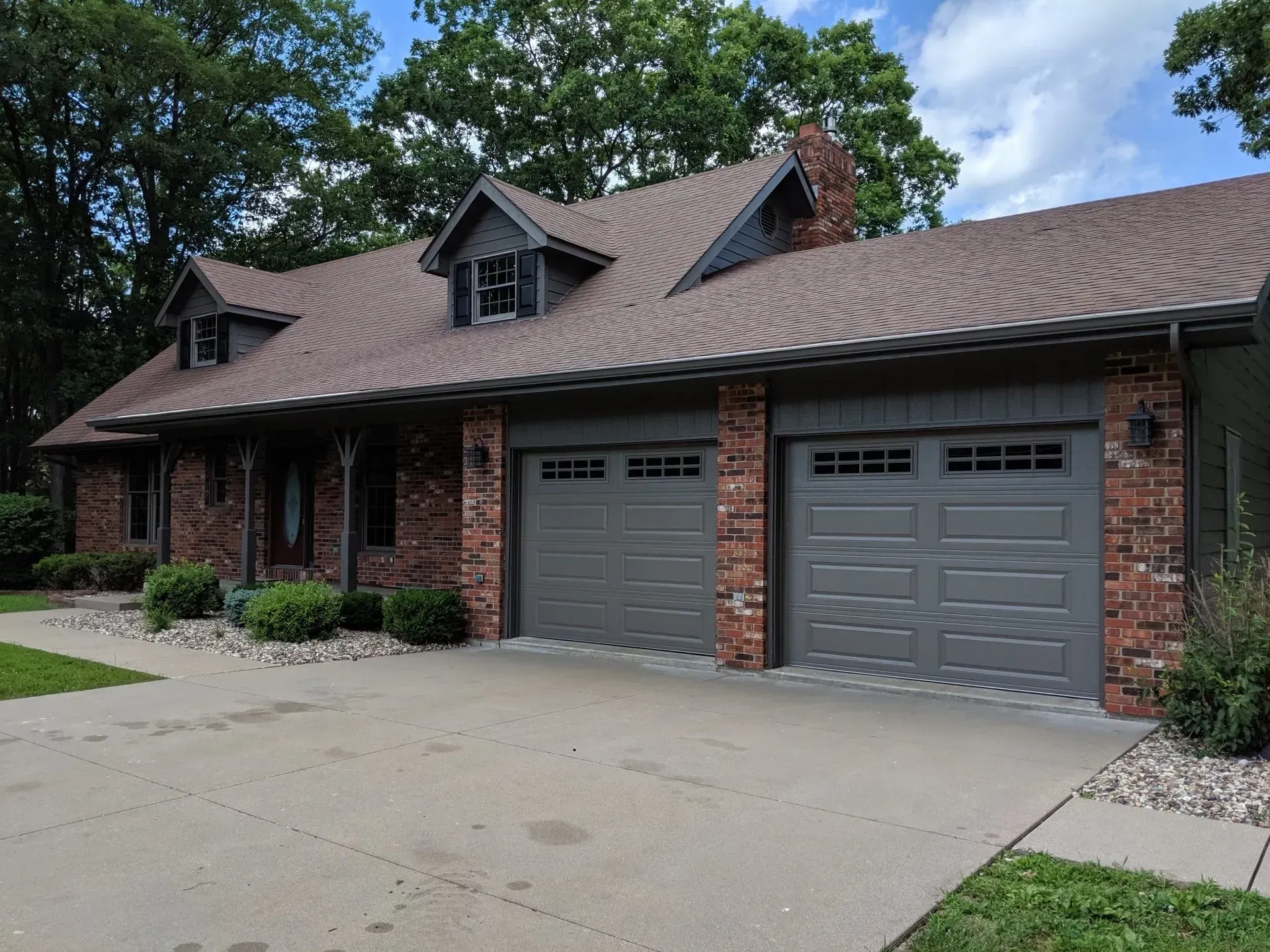 Brown brick house with gray garage doors and a concrete driveway.