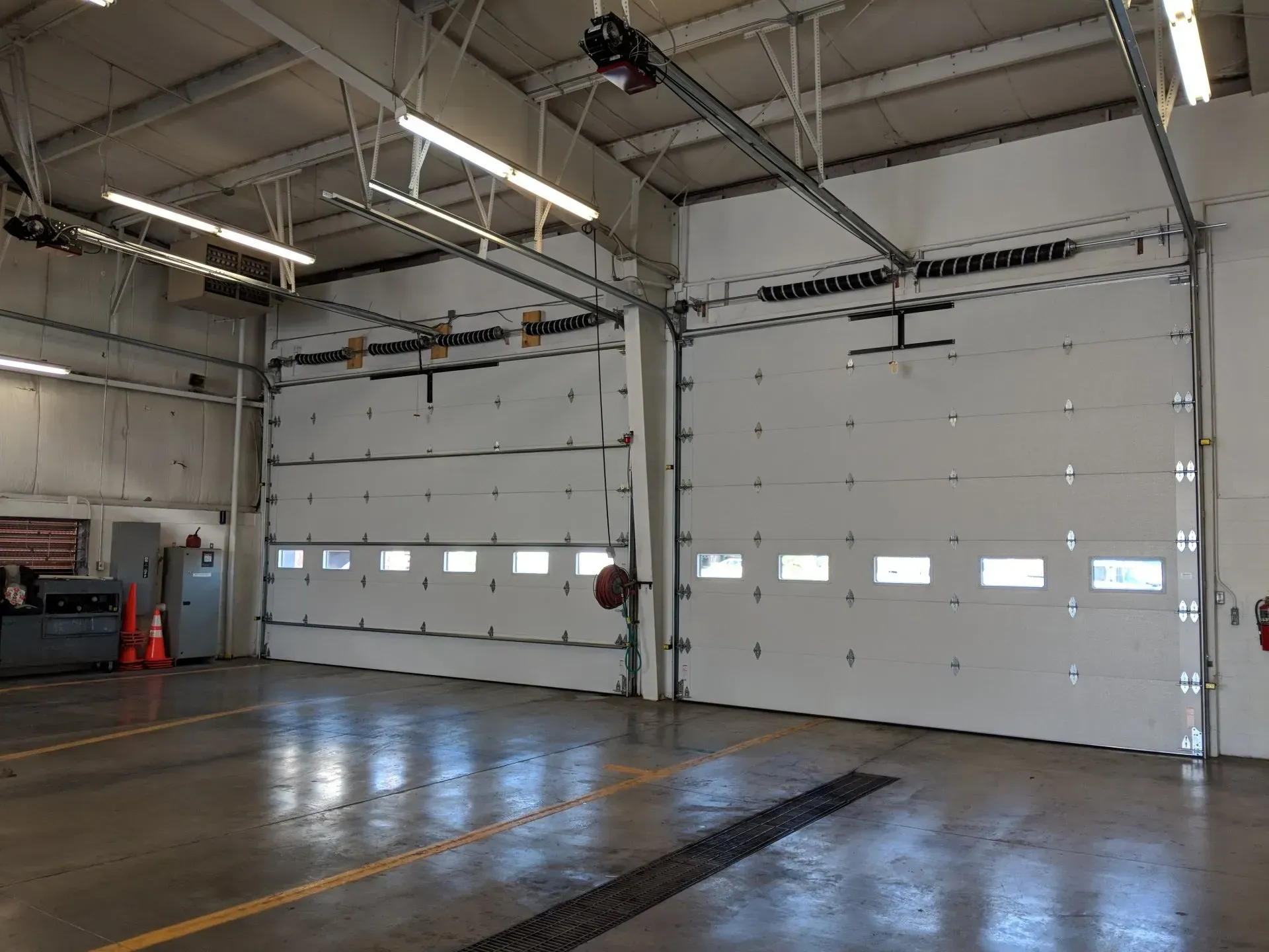 Two large, white garage doors inside a service bay, with overhead lighting.