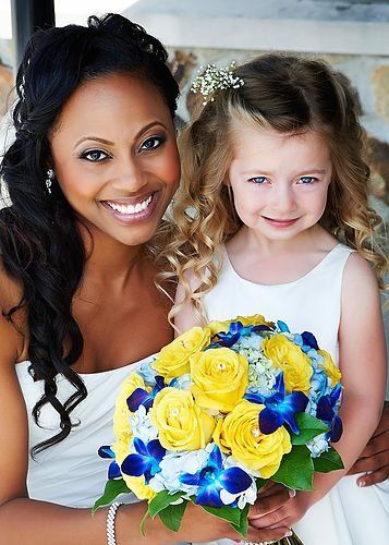 A woman in a white dress is holding a bouquet of yellow and blue flowers.