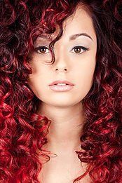 A woman with red curly hair is looking at the camera.