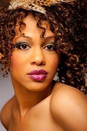 A woman with curly hair is wearing a feather headband.