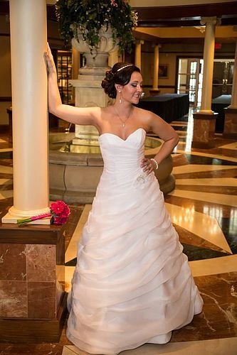 A woman in a wedding dress is leaning against a pillar.