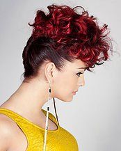 A woman with red curly hair is wearing a yellow tank top and earrings.