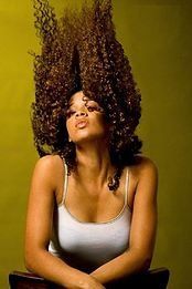 A woman with curly hair is sitting on a chair with her hair blowing in the wind.