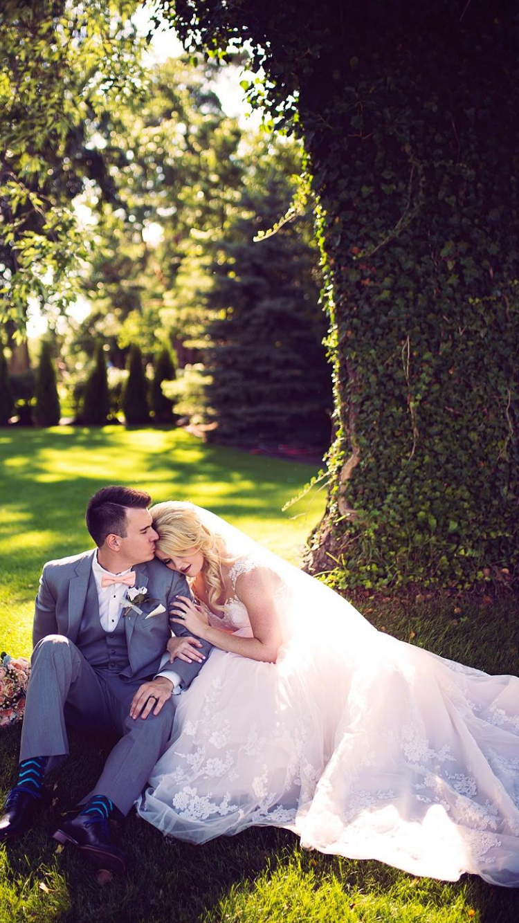 A bride and groom are sitting under a tree in the grass.