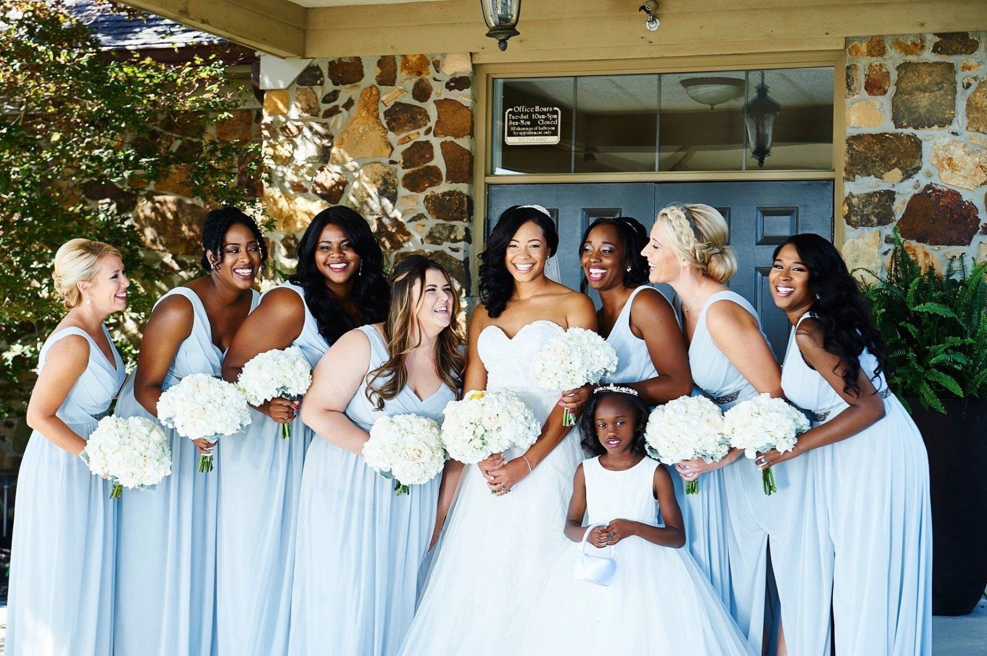 A bride and her bridesmaids pose for a picture in front of a stone building