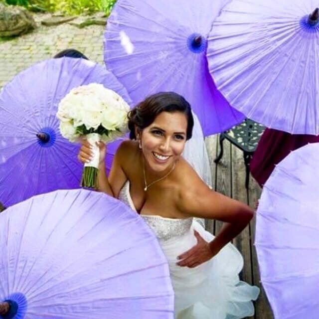 A woman in a white dress is surrounded by purple umbrellas