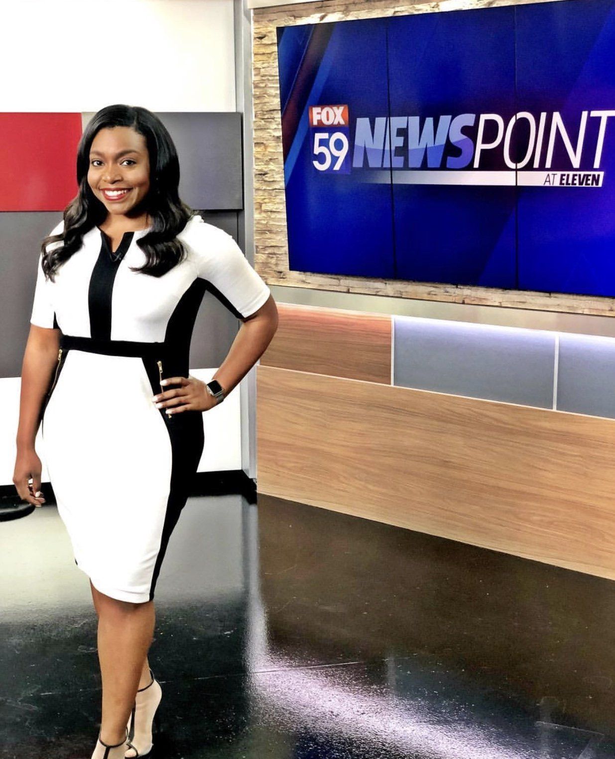 A woman in a black and white dress is standing in front of a fox 59 news point sign