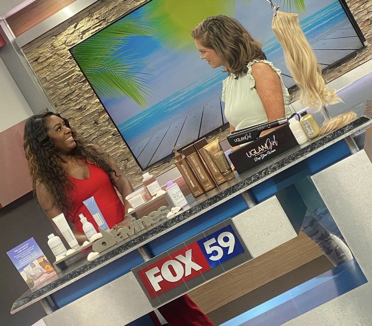 Two women are sitting at a table in front of a fox 59 sign.