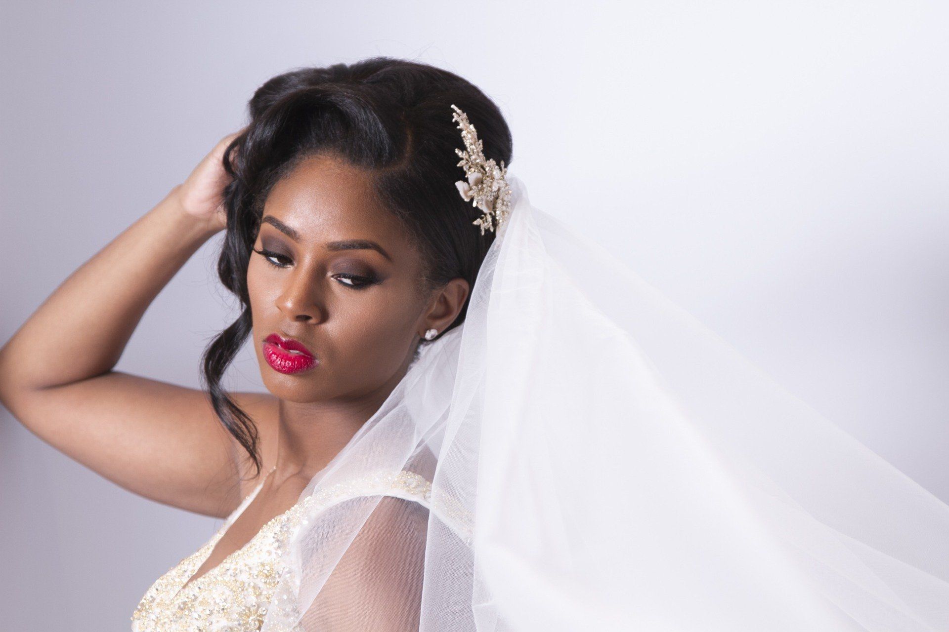 A woman in a wedding dress and veil is holding her hair.