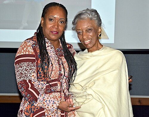 Two women smiling, one holds a trophy
