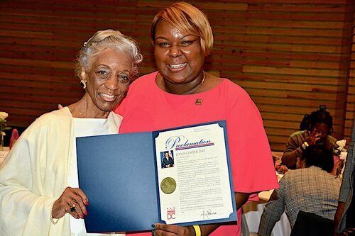 Woman in pink dress presents certificate to older woman in cream attire