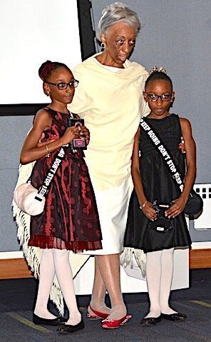 Woman in cream dress stands with two girls in formal dresses