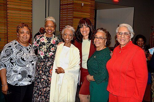 Group of six women smiling, posing for a photo at an event