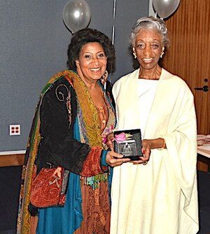 Two women pose, one presents a framed gift