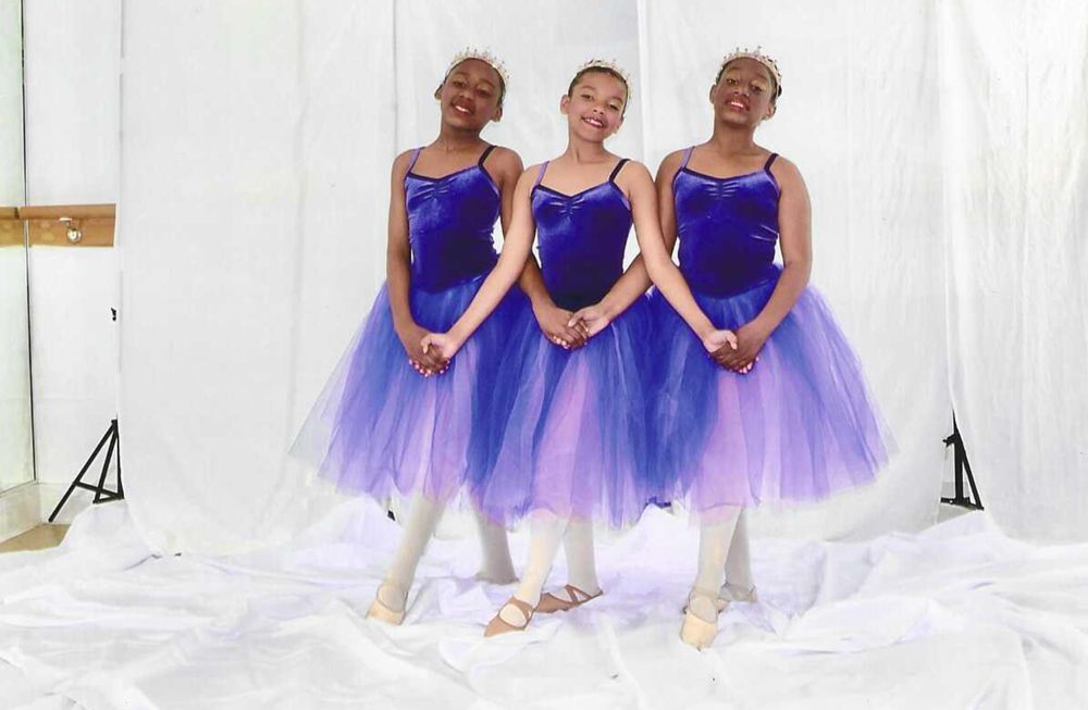 Three ballet dancers in blue tutus and tiaras pose in a studio.