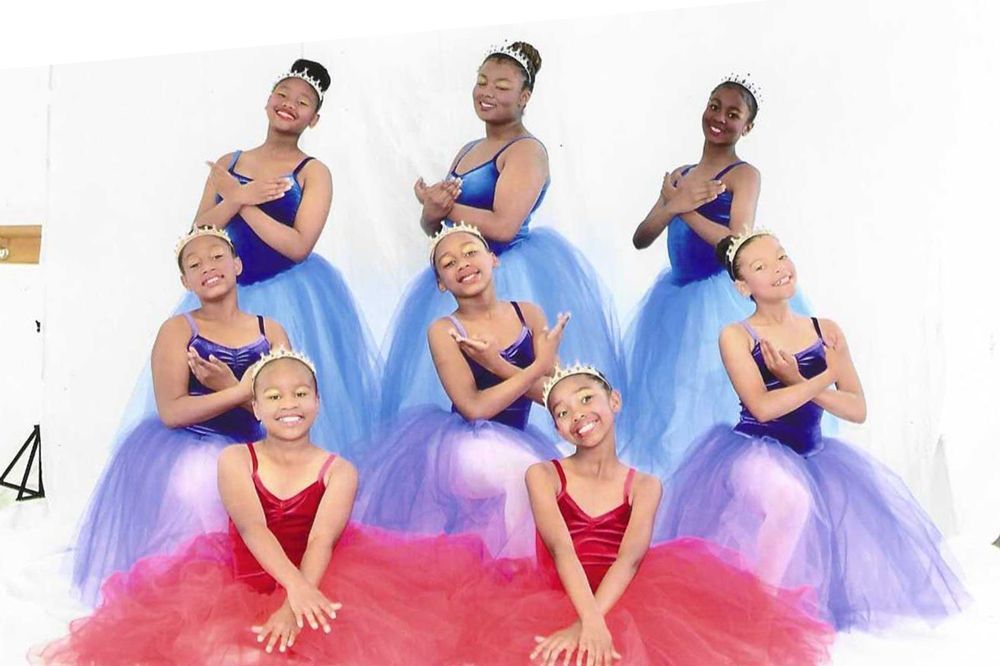 Ballet dancers in colorful tutus and tiaras pose against a white backdrop.