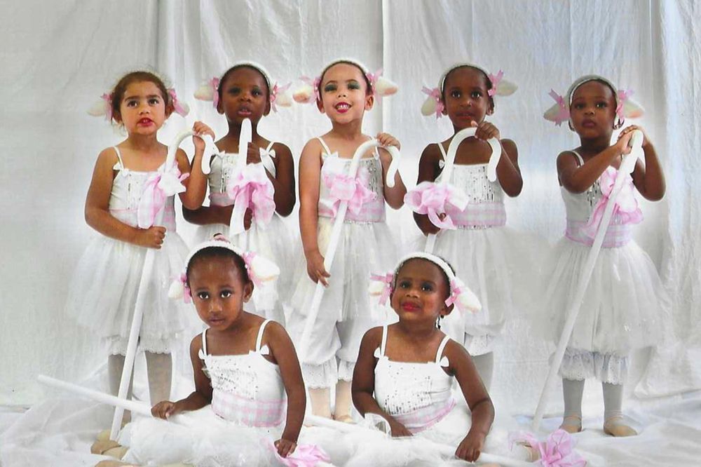 Group of children in white dresses, lamb ear headbands, and holding staffs, pose for photo.
