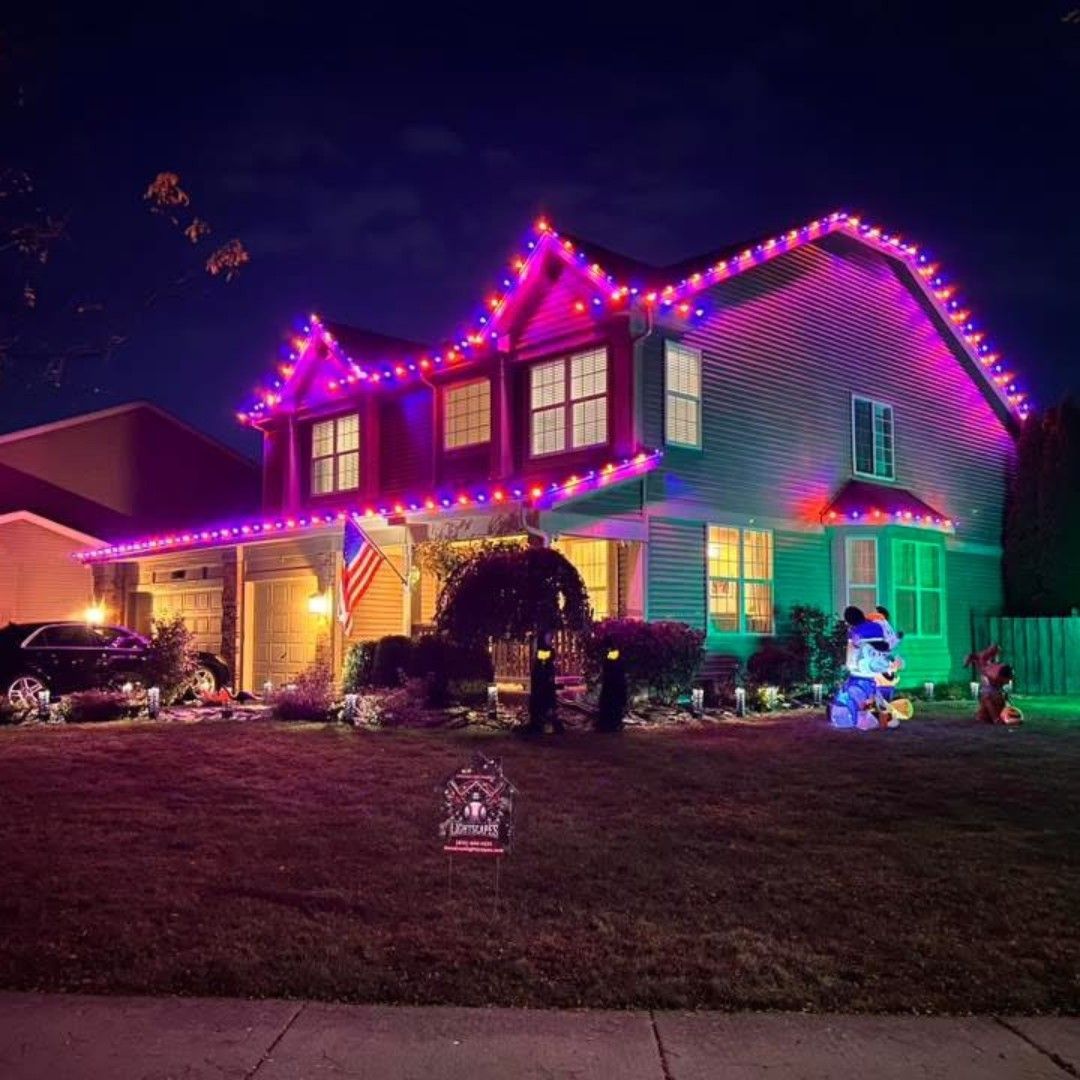 A two-story house illuminated with pink, red, and green lights for a holiday.