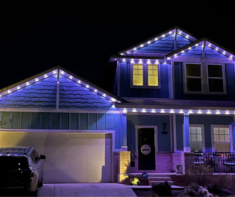 House at night with blue lights on the roof, garage, and front porch. A car is parked in the driveway.