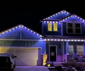 Blue house at night, illuminated by purple and white lights along the roof and trim.