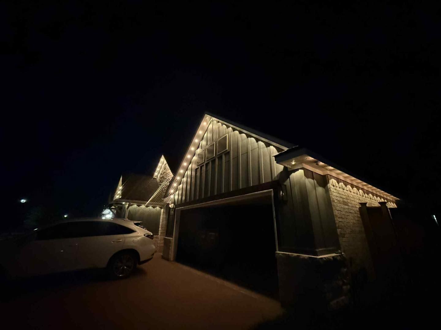 House at night with roofline lit by strings of small lights. A car is parked in the driveway.