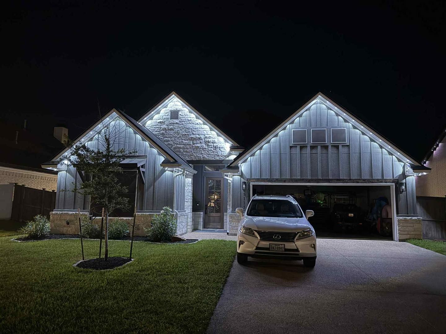 Night view of a house with white lights outlining the roof; a car is parked in the driveway.