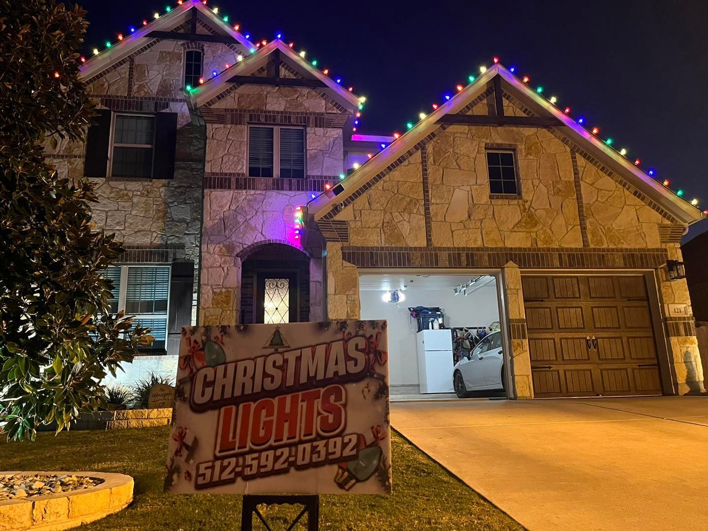 House with colorful Christmas lights, sign advertising Christmas lights with phone number.