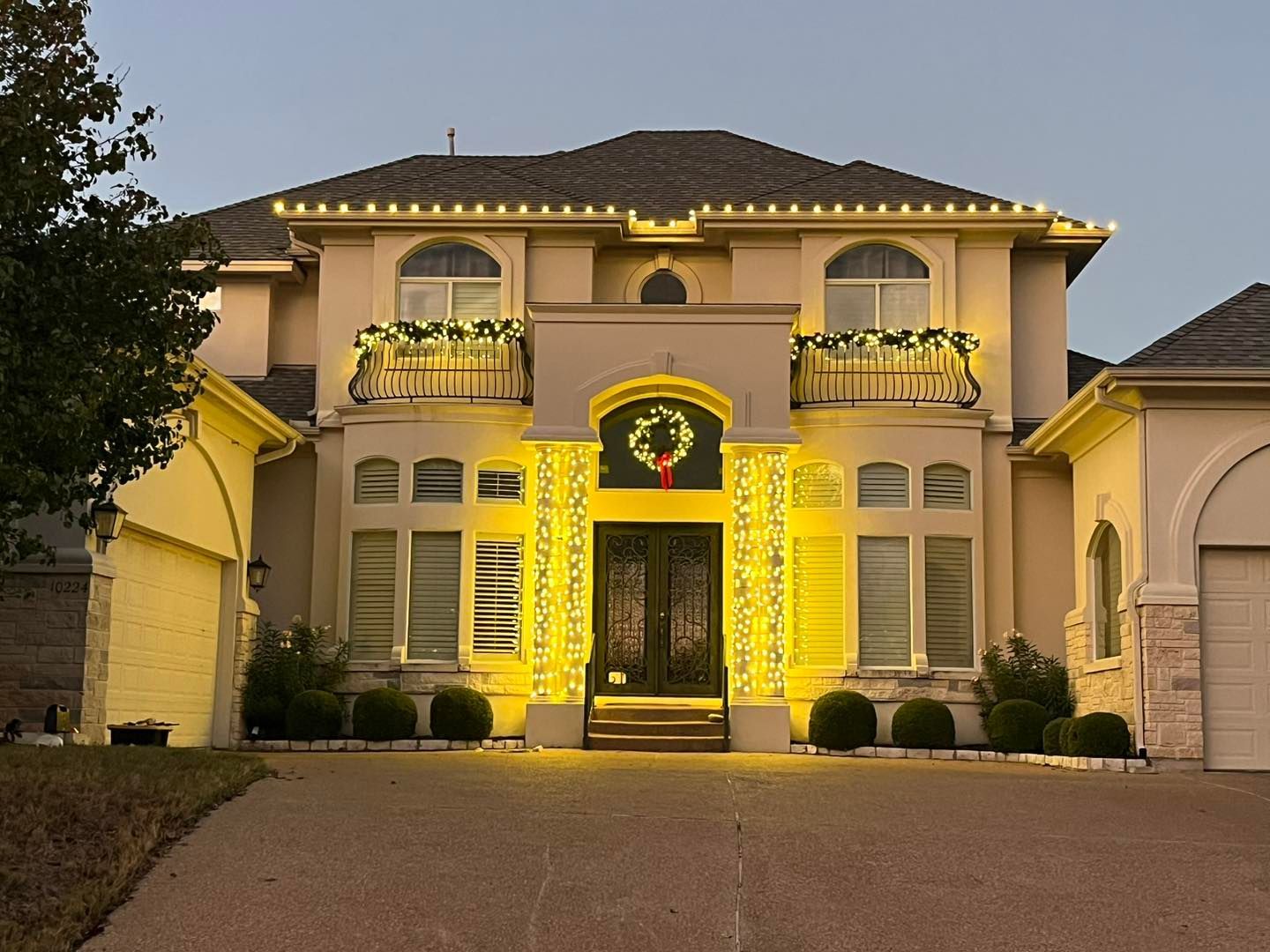 Elegant house decorated with yellow Christmas lights, garland, and wreaths.