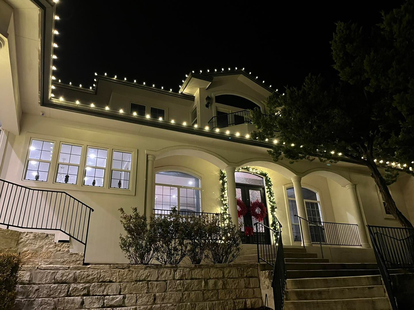 A white house at night with Christmas lights on the roof, windows, and around the front door.