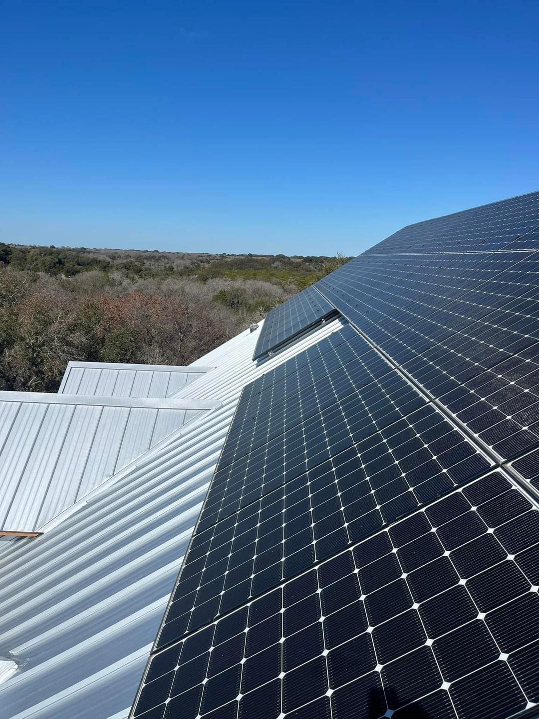 Solar panels installed on a corrugated metal roof against a backdrop of trees and a blue sky.
