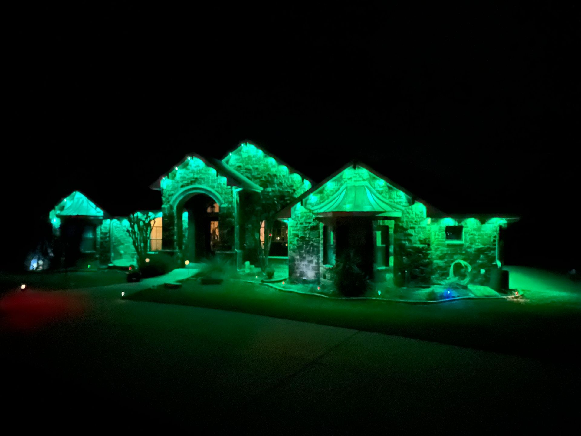 House with Christmas lights along rooflines; sign advertises holiday lighting services.