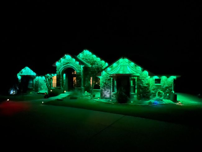 House with Christmas lights along rooflines; sign advertises holiday lighting services.