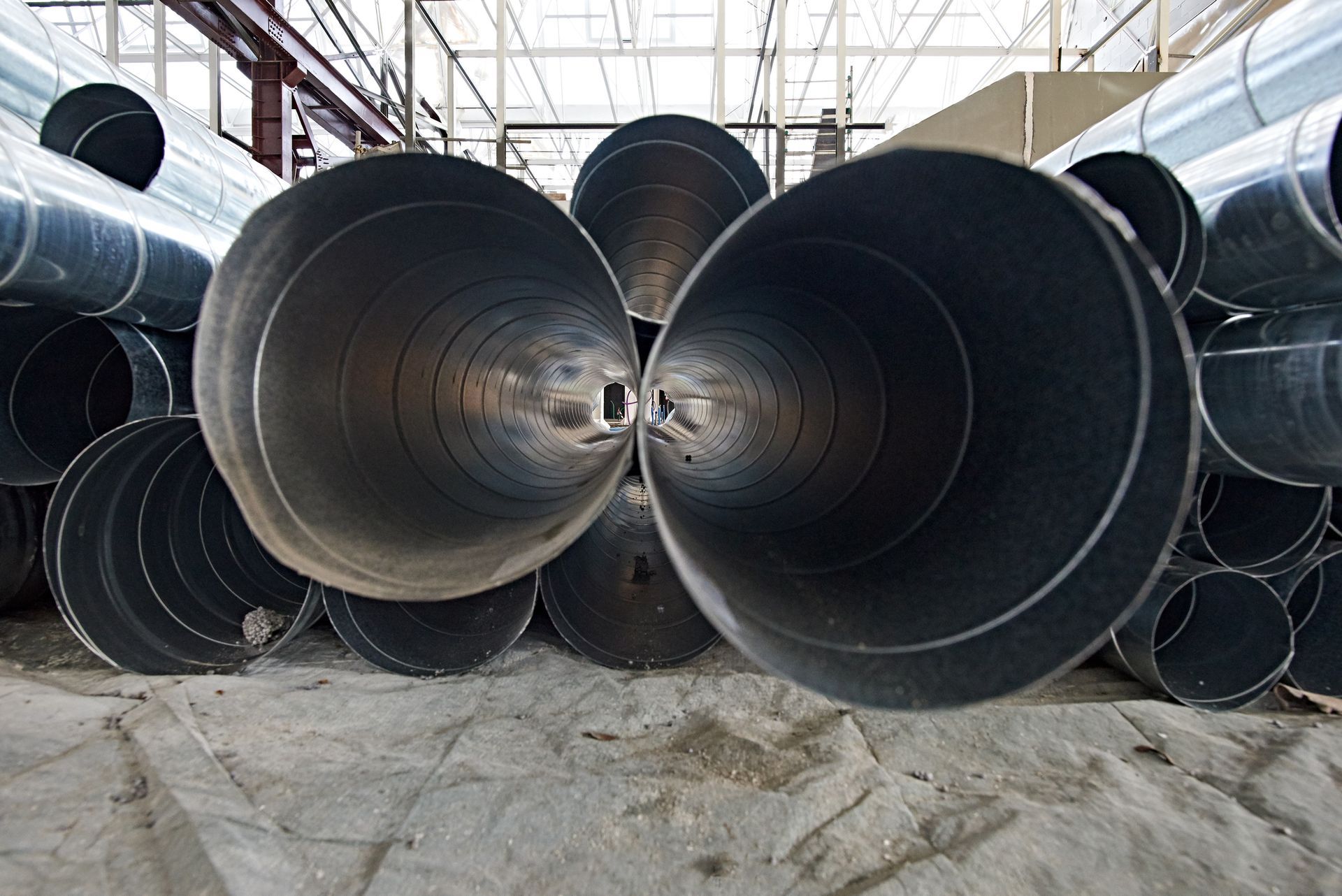 Metal pipes for ventilation, placed on the ground in a construction site.