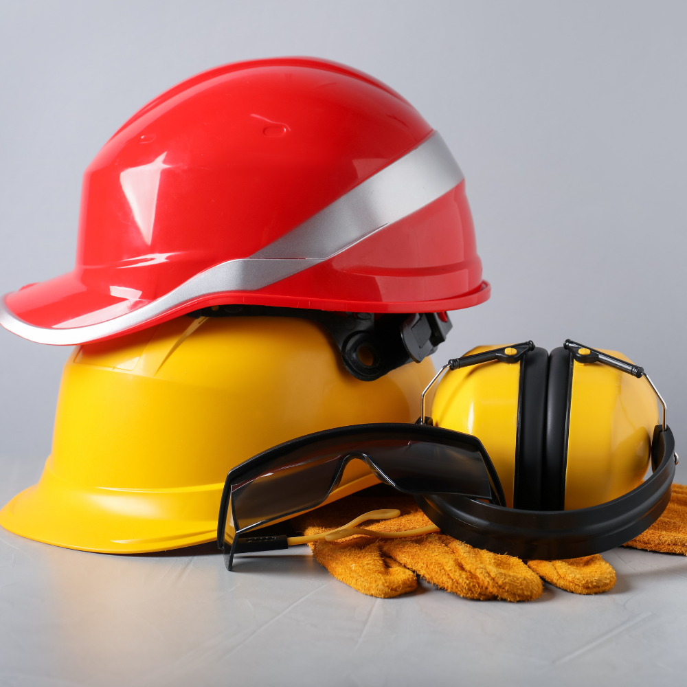 Red and yellow hard hats with safety goggles and work gloves on a gray surface