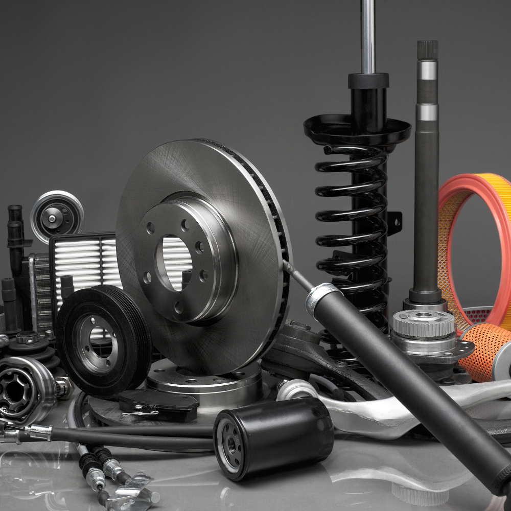 Assorted car parts and tools on a gray surface, including a brake disc, springs, belts, and pulleys