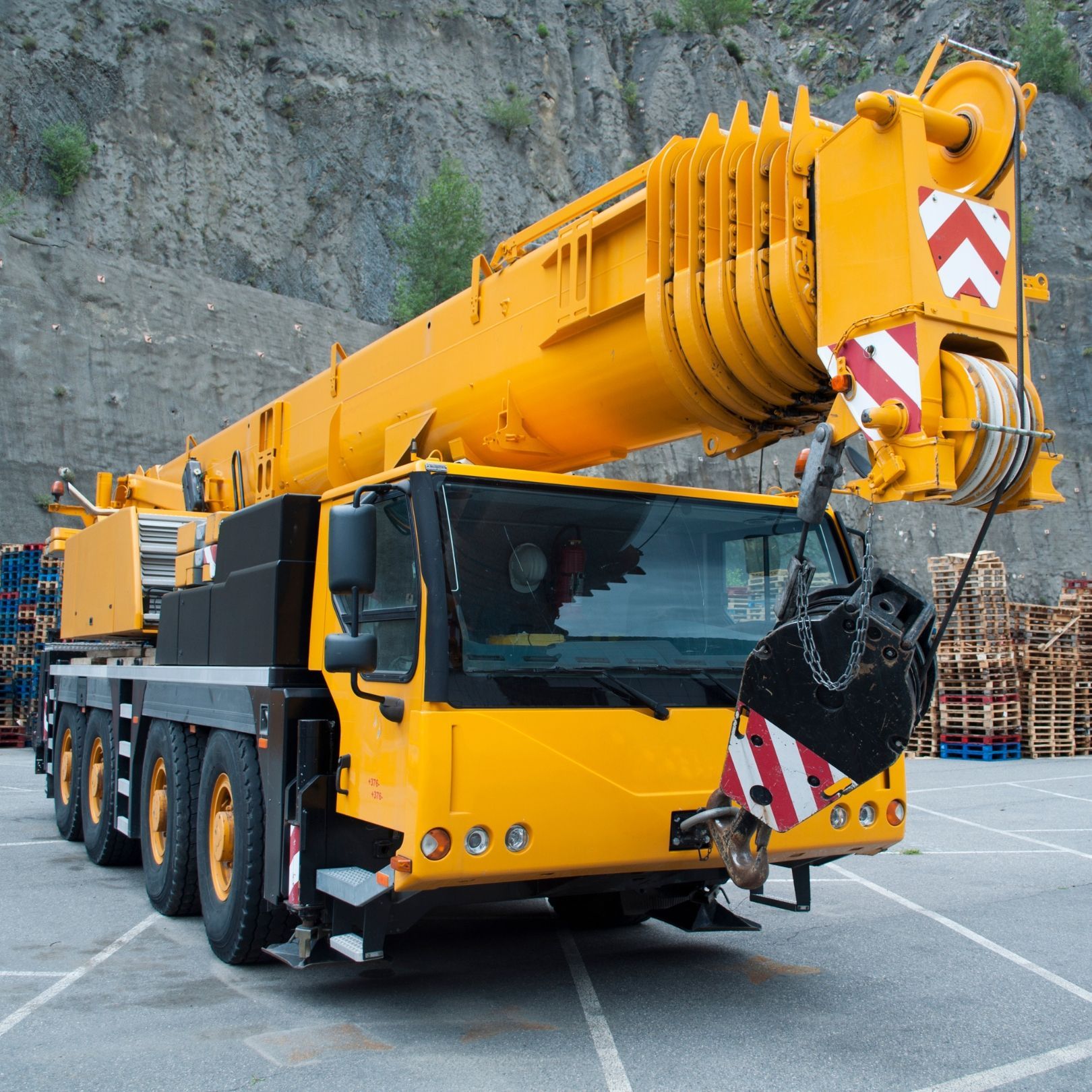 Yellow mobile crane truck on a construction site with a rocky cliff backdrop