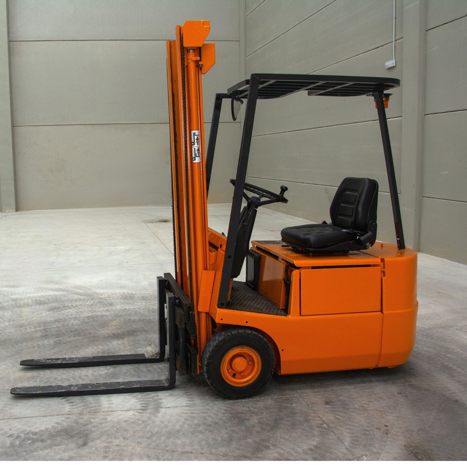 Orange forklift truck with black seat and overhead guard, shown in a warehouse setting.