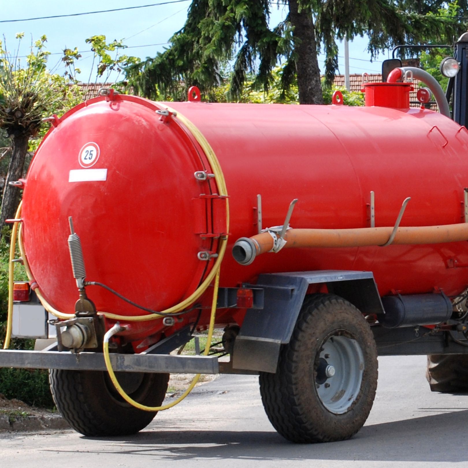 Red tanker truck parked on a street, with a bright red cylindrical tank and large wheels.