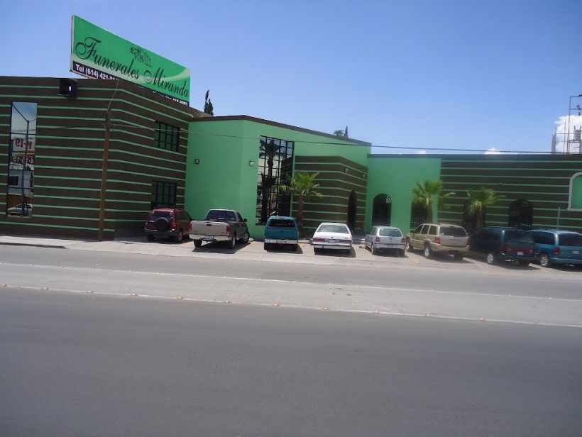 Una fila de coches están aparcados delante de un edificio verde.