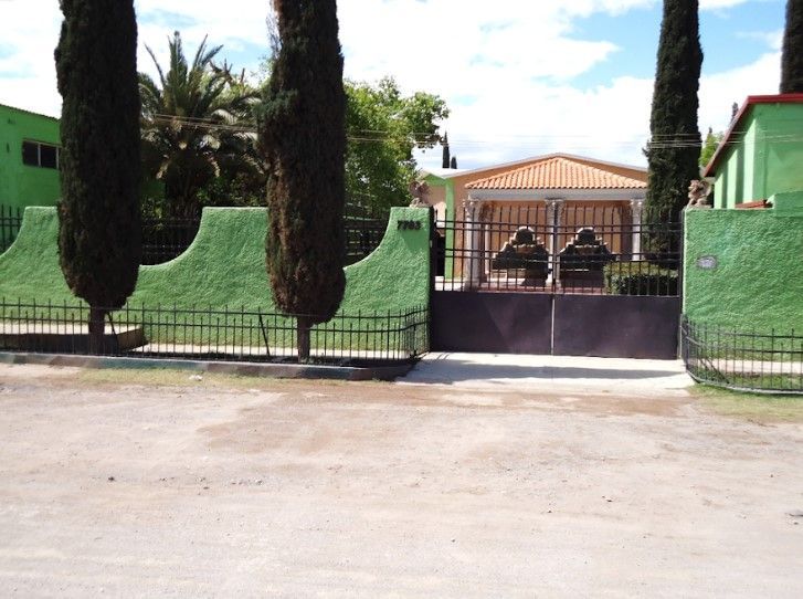 Una casa con una cerca verde y árboles delante de ella.