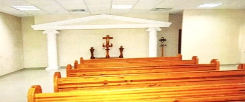 Una fila de bancos de madera en una iglesia vacía con una cruz en la pared.
