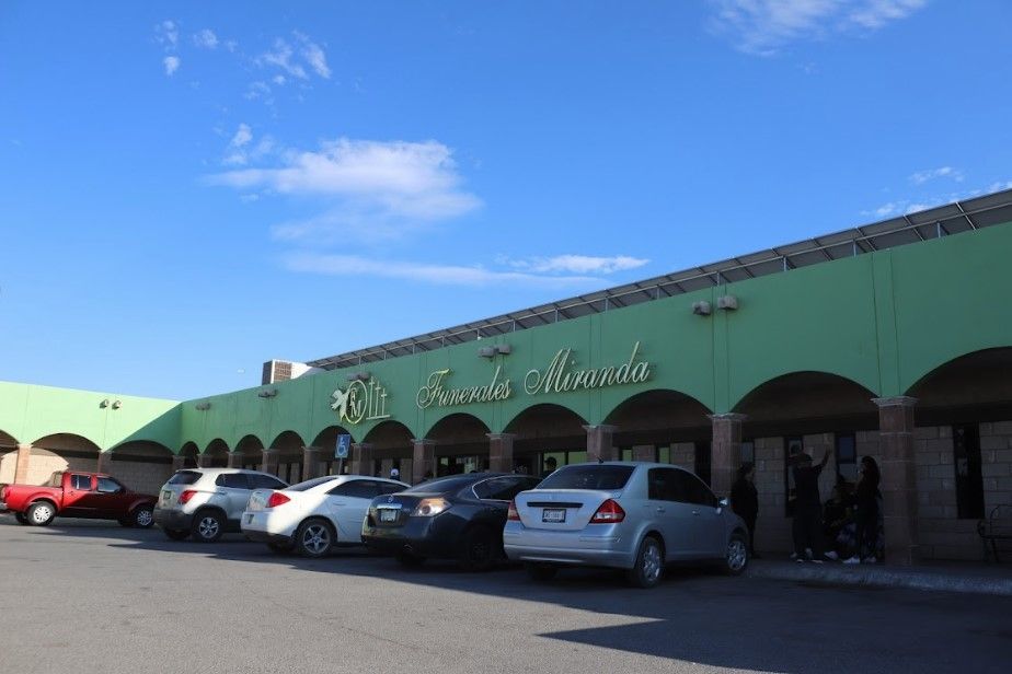 Una fila de coches están aparcados delante de un edificio verde.