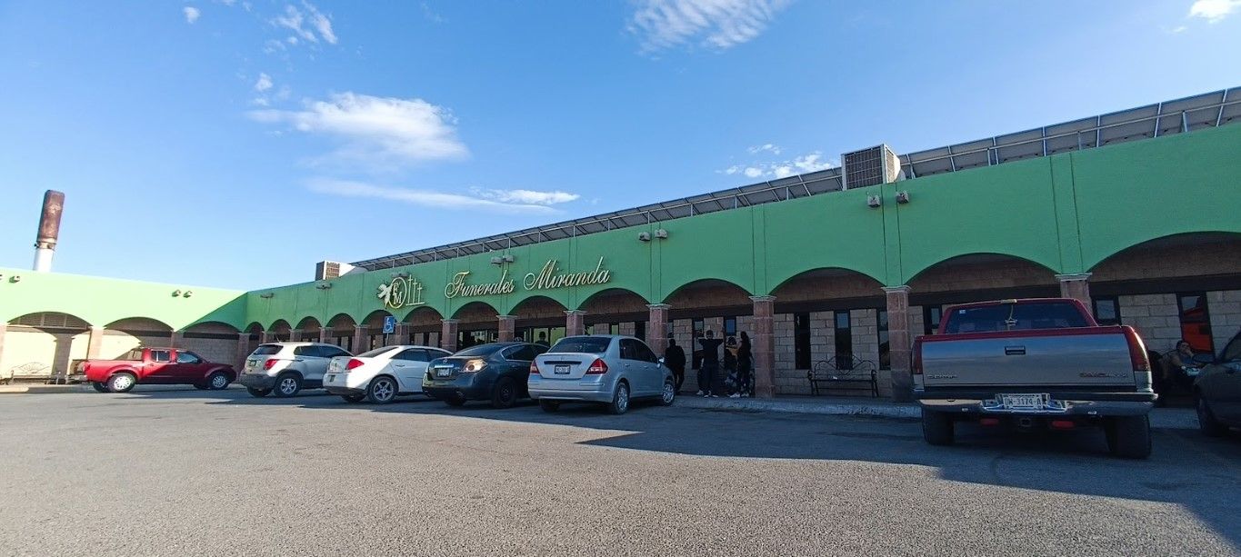 Una fila de coches están aparcados delante de un edificio verde.