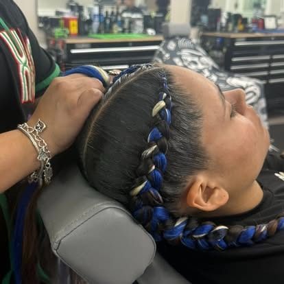 Person getting braids with blue and white hair extensions in a salon.